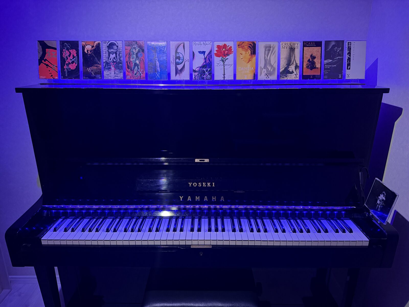 A YAMAHA upright piano engraved with YOSEKI, topped with a collection of X JAPAN CD singles